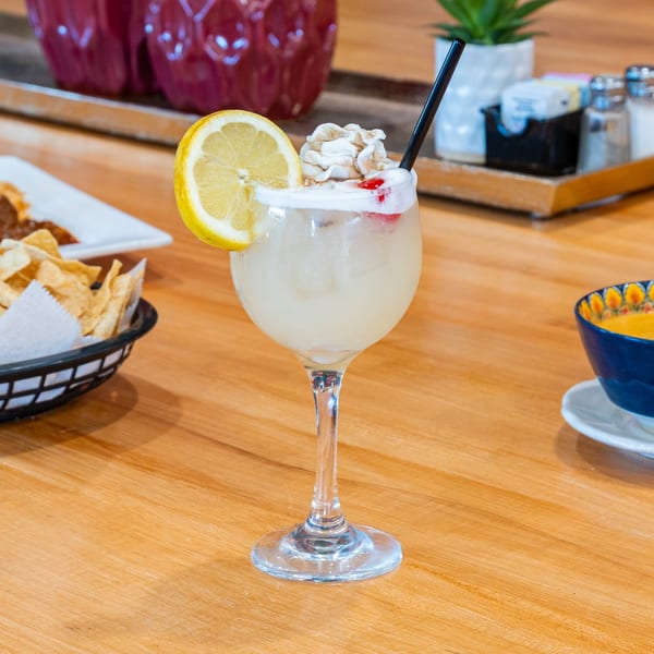 A refreshing Plano Tortilla Factory drink with lemon, whipped cream, and a straw on a wooden table.