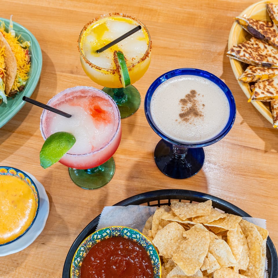 Overhead view of Plano Tortilla Factory's Mexican food spread: tacos, quesadillas, margaritas, chips, salsa, and queso.