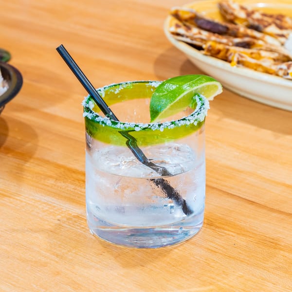 A refreshing margarita with a salted rim and lime wedge, next to a plate of quesadillas.