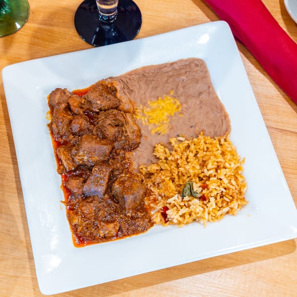 Plano Tortilla Factory's carne guisada with rice and refried beans on a white rectangular plate.