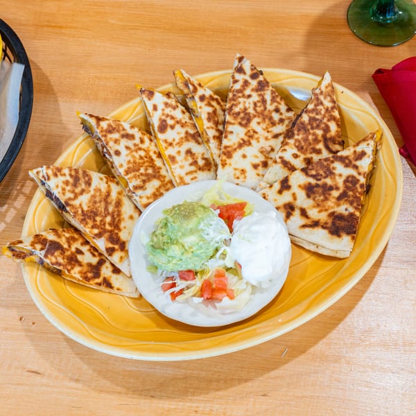 Plano Tortilla Factory's quesadillas with guacamole, sour cream, and pico de gallo on a yellow plate.