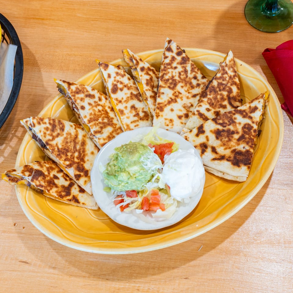 Plano Tortilla Factory's quesadillas with guacamole, sour cream, and pico de gallo on a yellow plate.