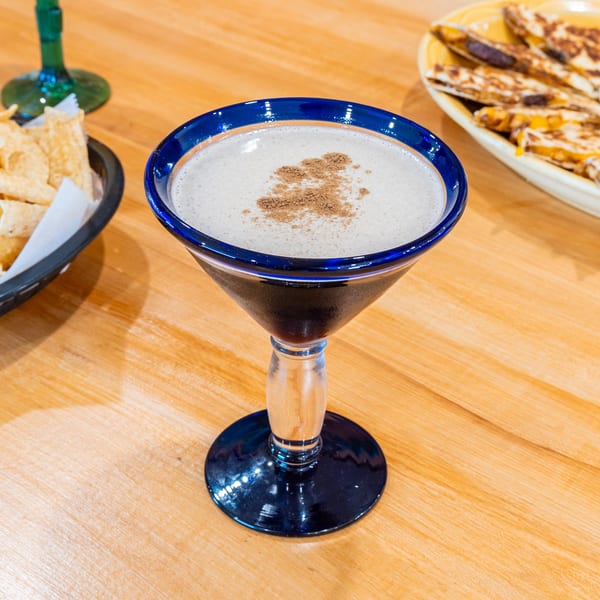 A horchata drink in a blue-rimmed glass with cinnamon, alongside chips and quesadillas.